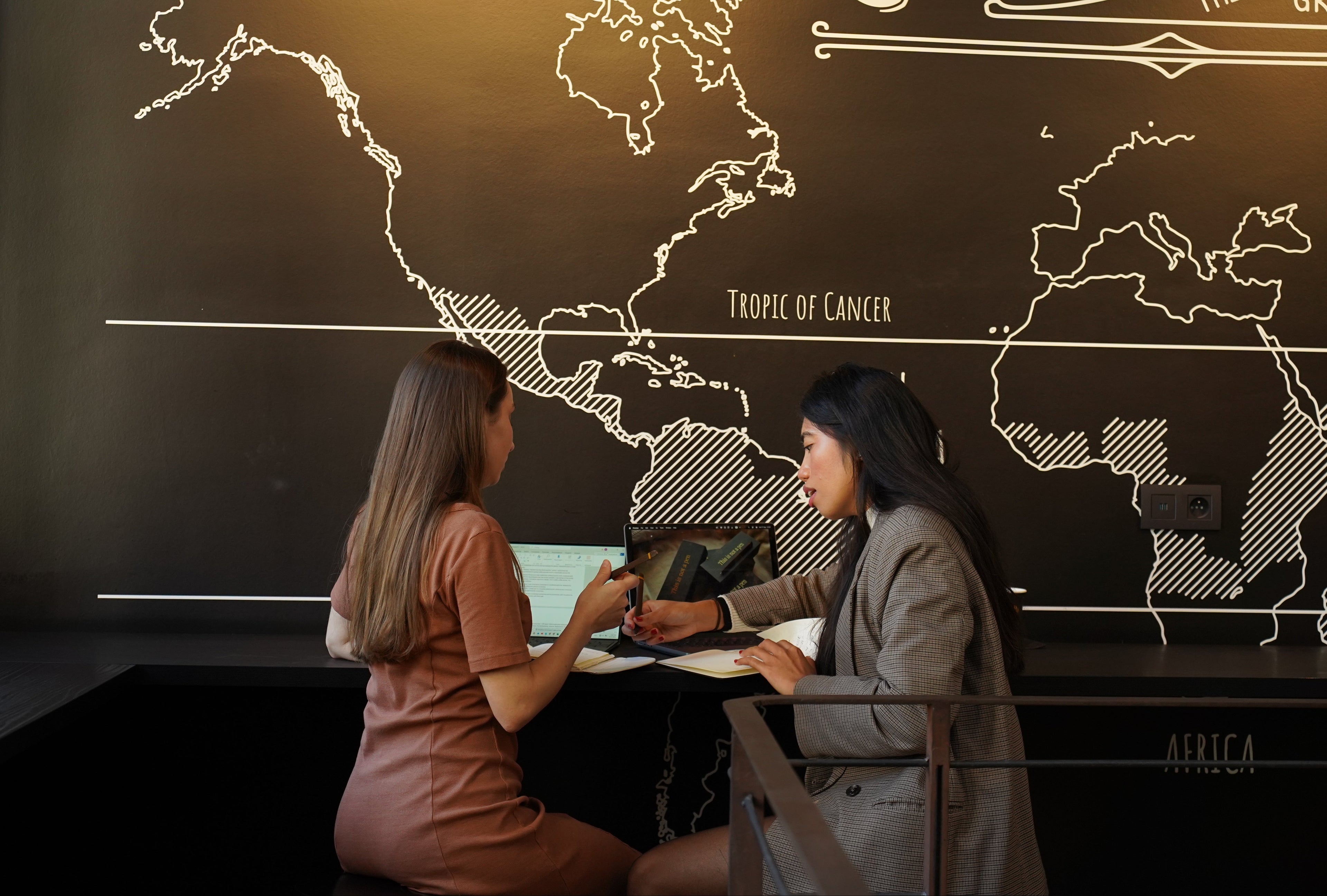Two women sitting at a table in front of a world map and coffee-themed decor.